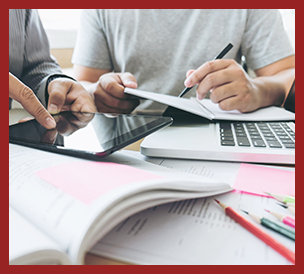 two people working with tablet, computer, workbooks and pencils