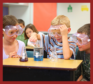 three students at desk wearing safety goggles doing science experiment